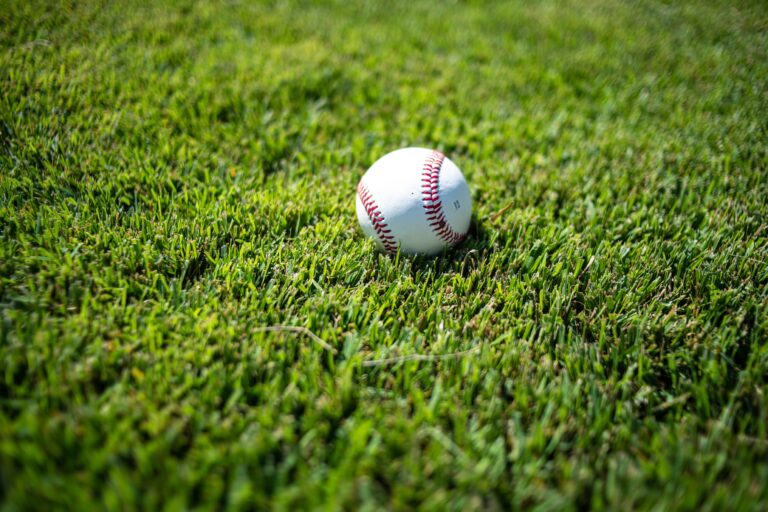 A white baseball with red stitching resting on lush green Zeon Zoysia grass