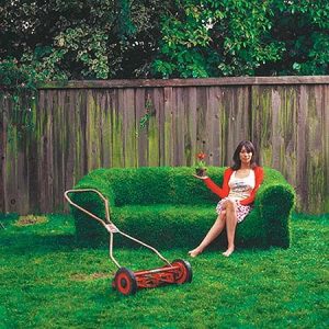 woman sitting on a grass couch with a push mower in front